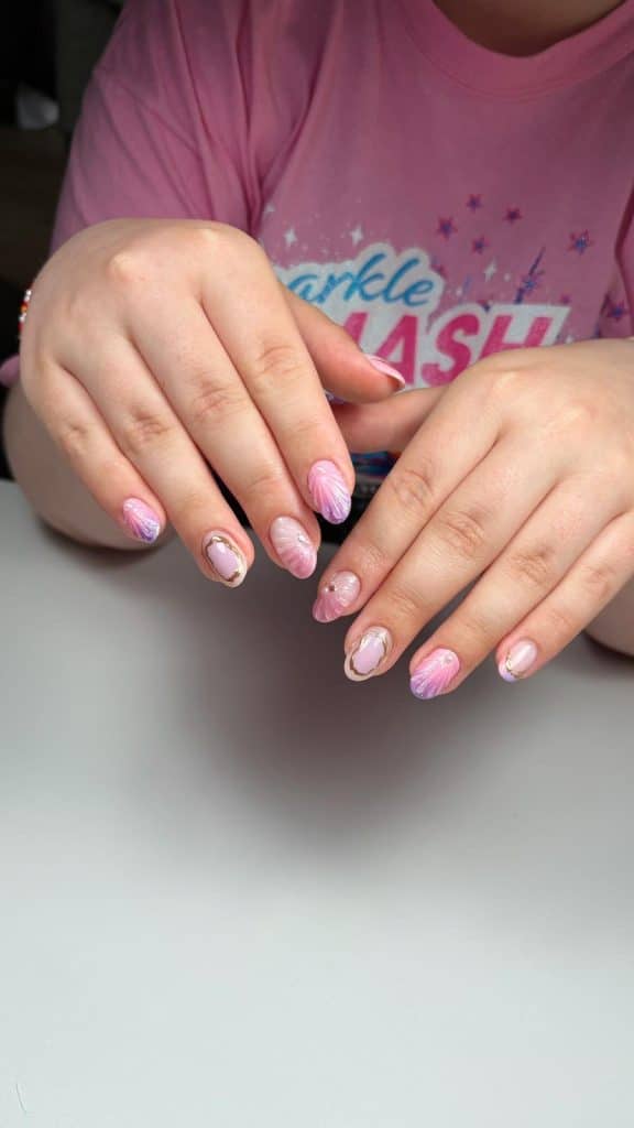Close-up of a girl's hands showing a pastel pink and lavender gradient manicure with delicate white swirls and tiny pearl accents on the nails.
